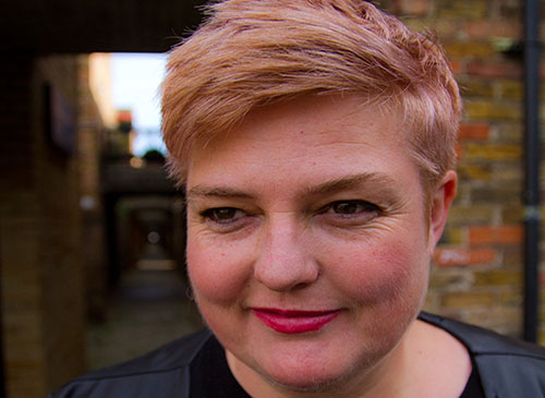 Portrait photograph of composer Jo Thomas infront of a brick building