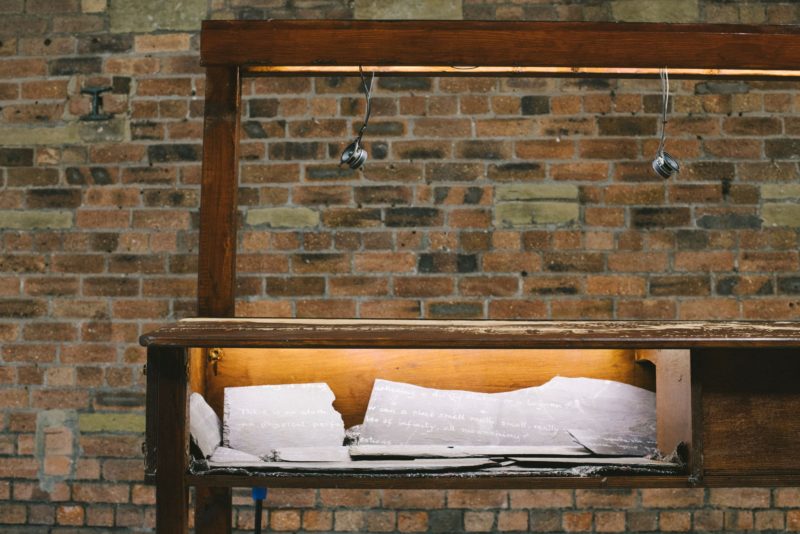 A wooden desk with lit up element underneath reveals slate with etchings on.