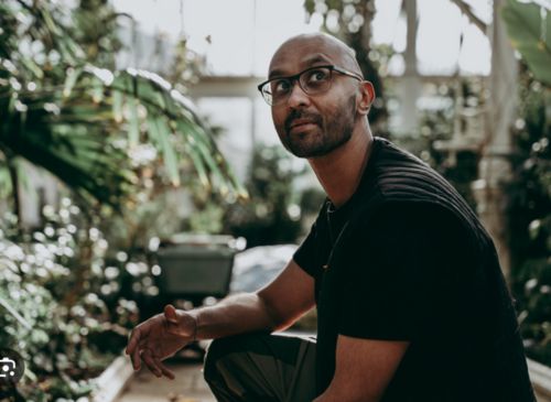 Man in greenhouse wearing black tshirt and kneeling near plants ( man is Jason Singh)